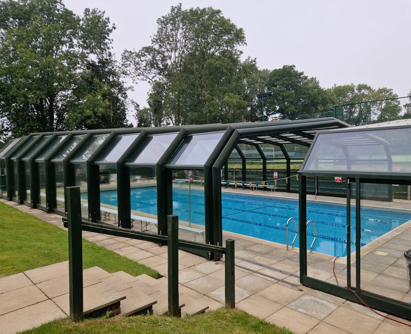 Curved glass swimming pool enclosure over an outdoor pool by Ace Pools